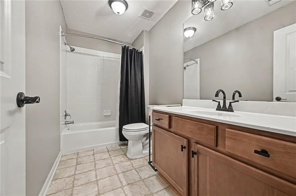 Bathroom with a wood vanity, white countertop, bathtub, and black shower curtain.