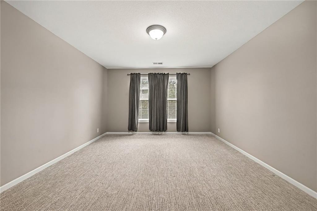 Empty carpeted bedroom with two curtained windows and a ceiling light.