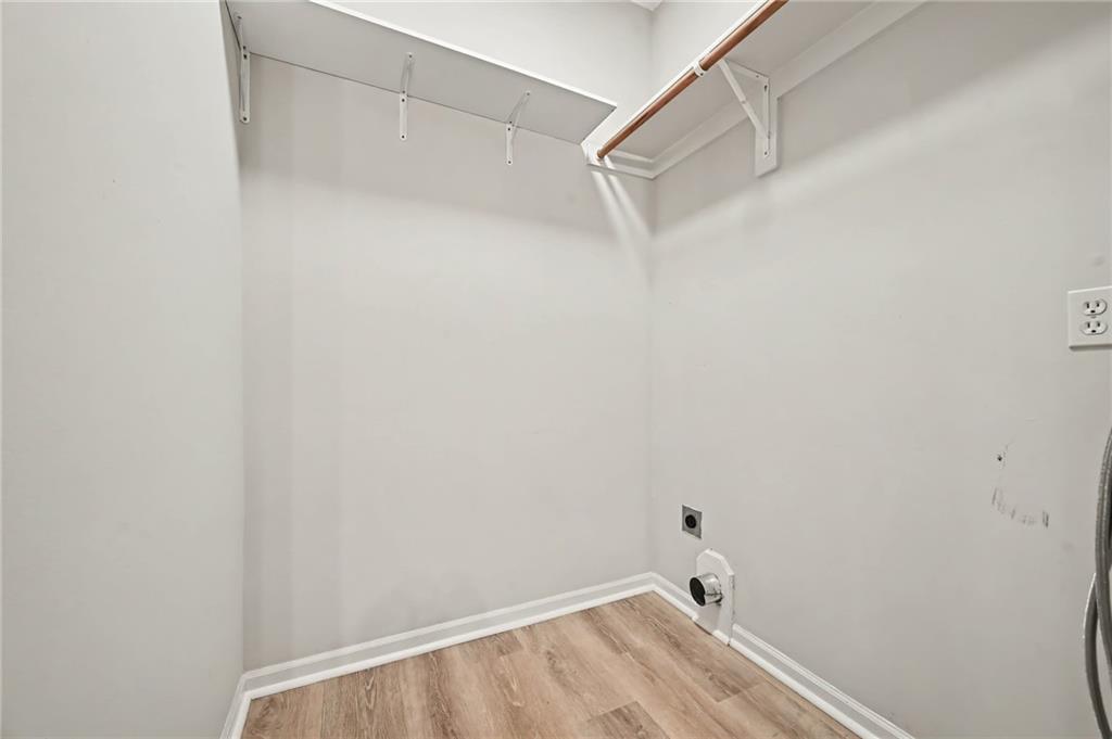 Empty laundry closet with upper shelving, a wooden hanging rod, and washer and dryer connections.