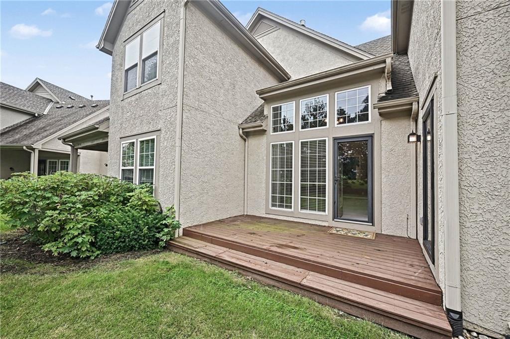 Rear of a stucco house with a raised wooden deck, tall windows, and a glass door.