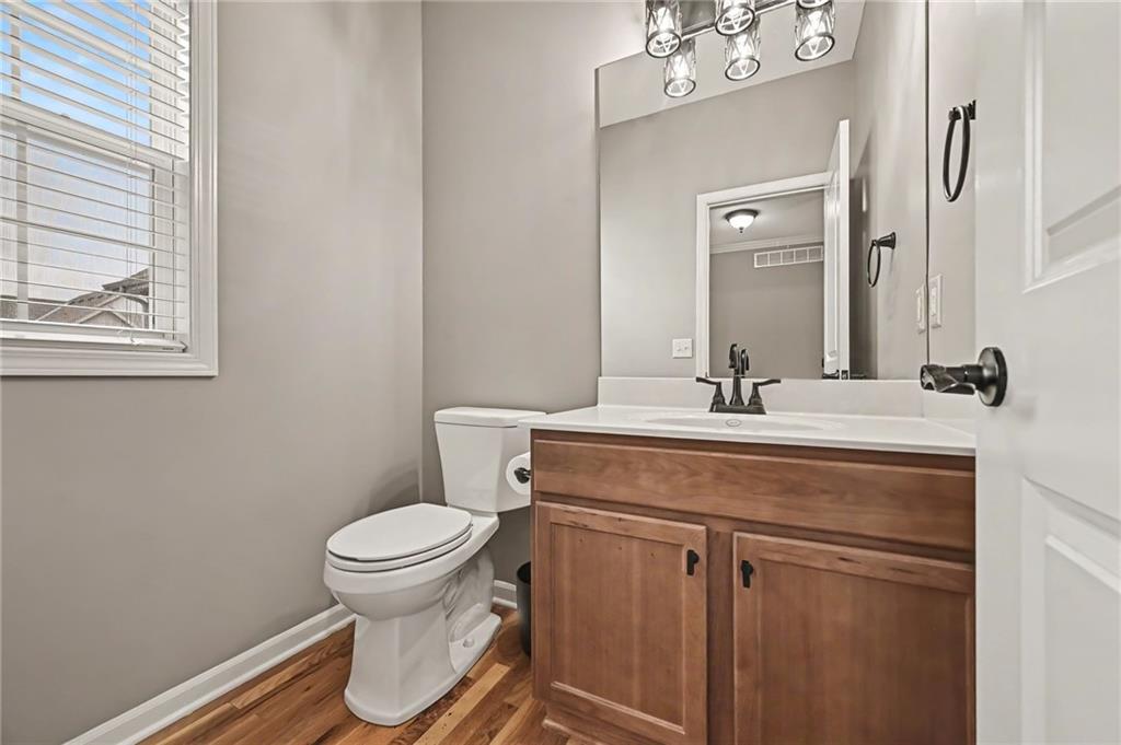 Bathroom with a wood vanity, large mirror, white toilet, and wood flooring.