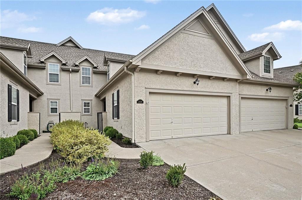 Beige attached home with white garage doors, a prominent front gable, and landscaped beds.