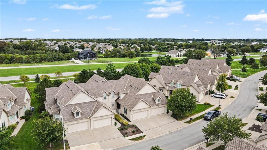 Aerial view of attached homes along a residential street, with green lawns and a neighborhood beyond.