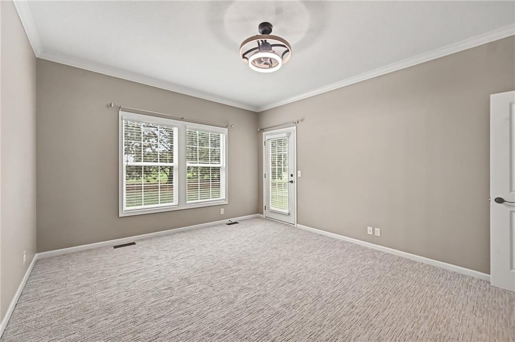 Empty carpeted room with wide windows, a glass exterior door, and a modern ceiling light.