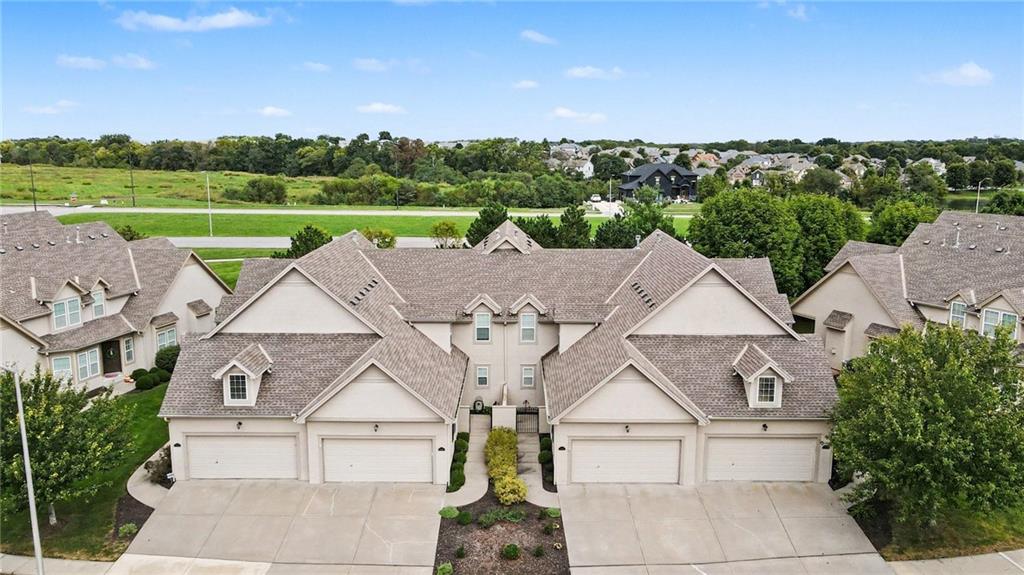 Aerial view of attached homes with gray roofs and garages beside a green open area.