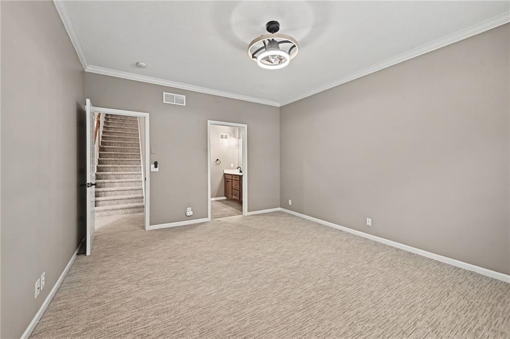 Empty carpeted room with gray walls, a ceiling light, and doorways to stairs and a bathroom.