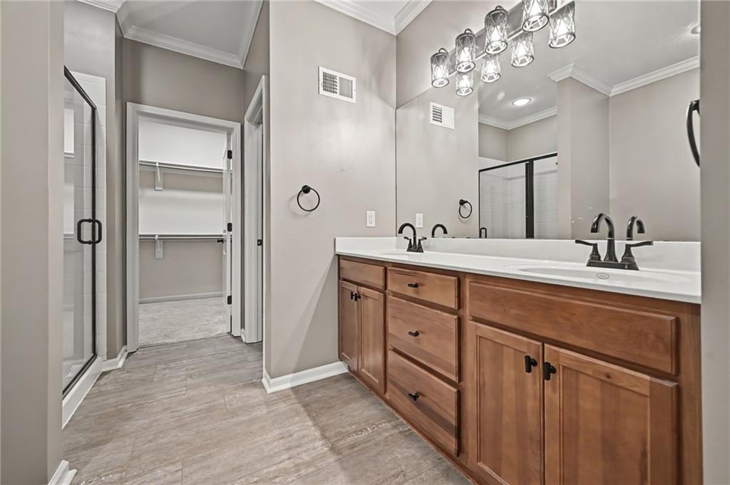 Bathroom with a double-sink wood vanity, large mirror, and glass shower beside an open walk-in closet.