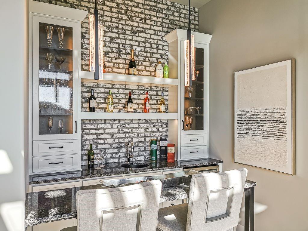 Home bar with white brick backsplash, glass-front cabinets, and upholstered counter chairs.
