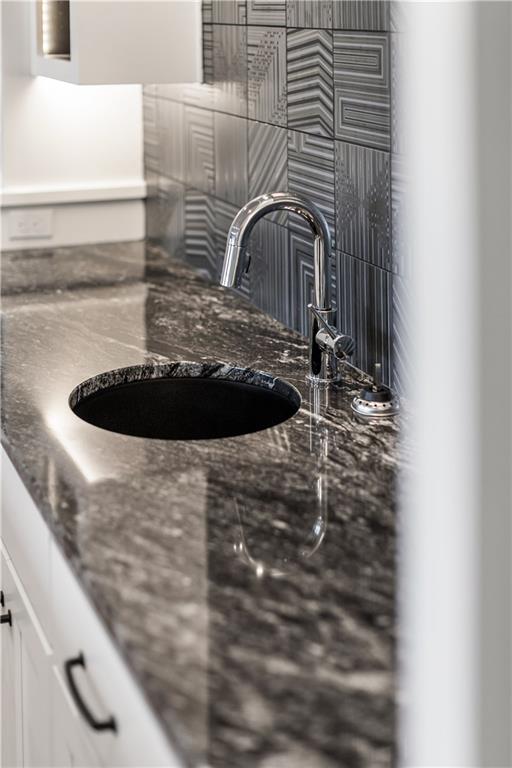 Bathroom vanity with a round black sink, dark stone counter, chrome faucet, and patterned gray tile backsplash.