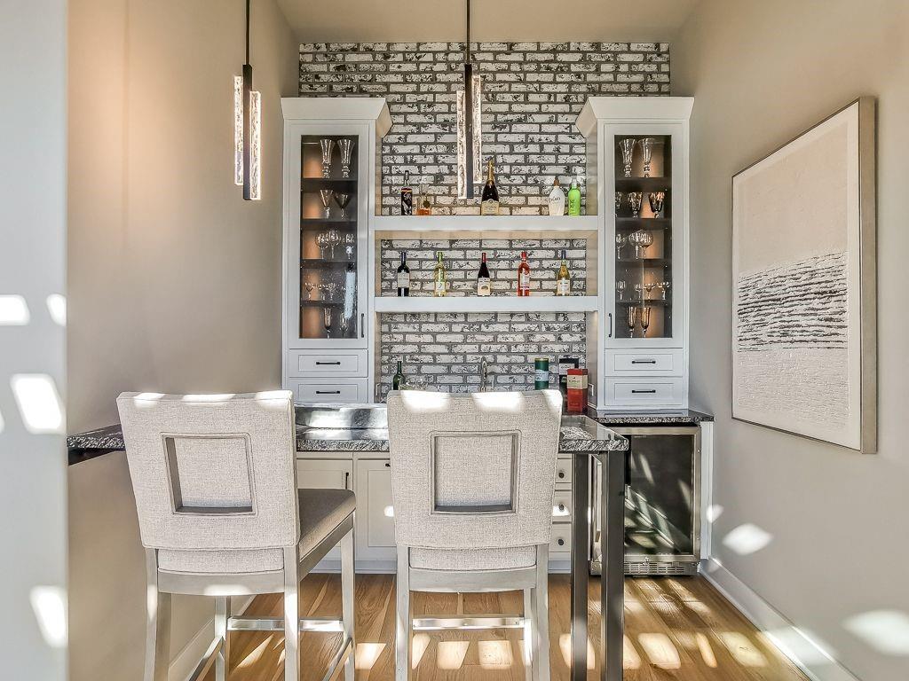 Home bar with white brick backsplash, built-in glass-front cabinets, and two upholstered counter stools.