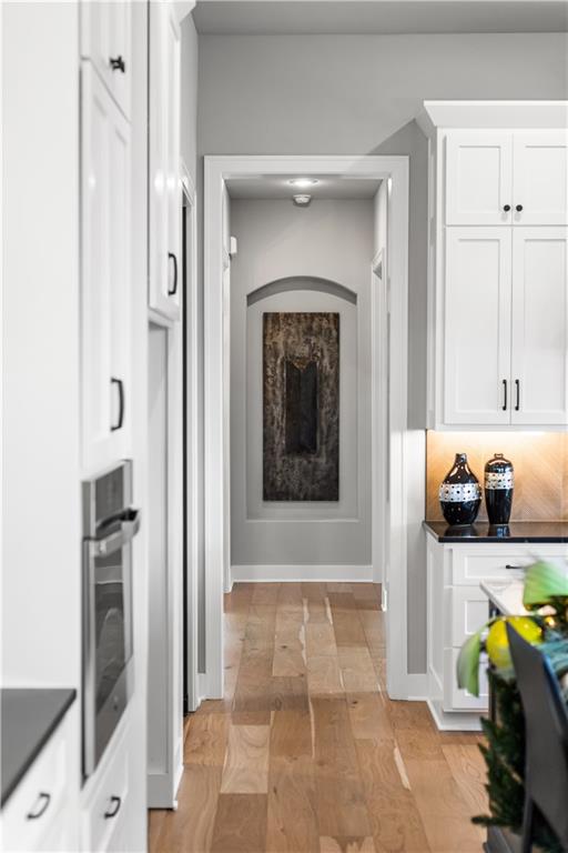 White kitchen with hardwood floors, built-in oven, and a hallway displaying framed artwork.