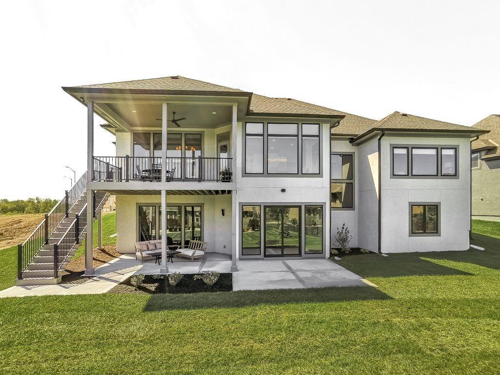 Rear exterior of a two-story home with an elevated deck, patio, and broad lawn.