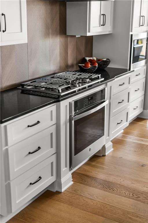 Kitchen with white cabinetry, black counters, stainless steel appliances, and light hardwood floors.