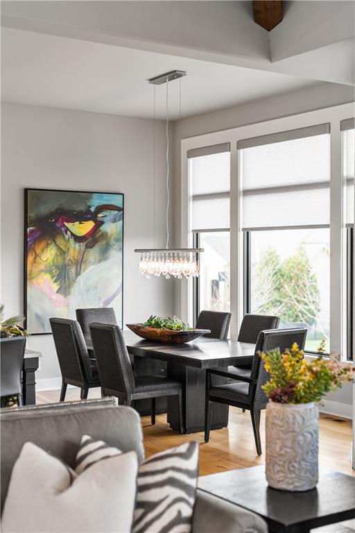 Dining room with a dark table, crystal chandelier, tall windows, and colorful abstract artwork.