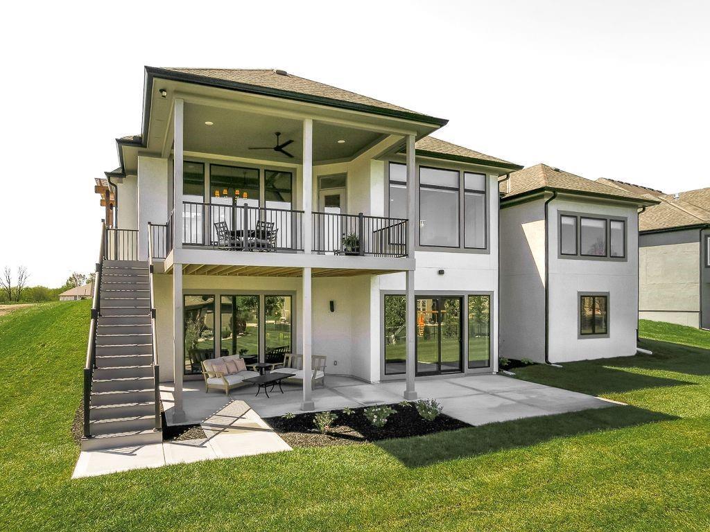 Rear of a modern home with a covered balcony, exterior stairs, and furnished patio.
