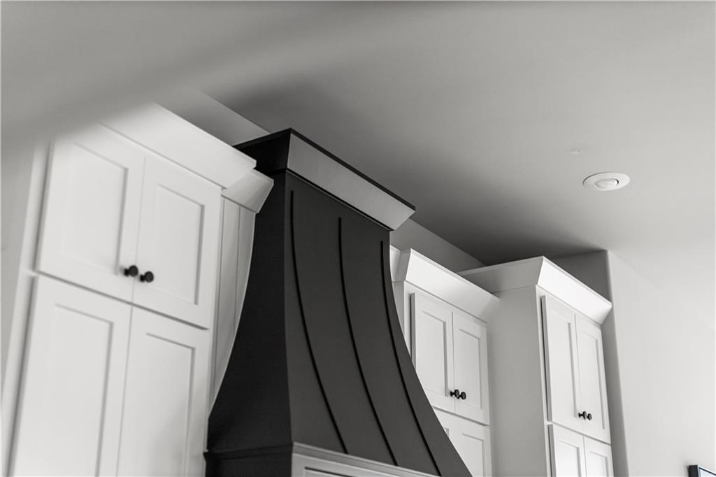 Kitchen with a dark sculptural range hood between white paneled cabinets.