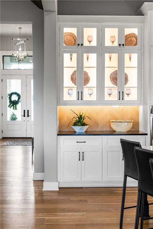 Dining area with white glass-front cabinets and an illuminated serving counter beside dark chairs.