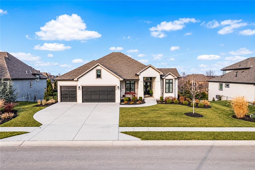 Single-story home with two dark garage doors, a broad driveway, and a landscaped front lawn.