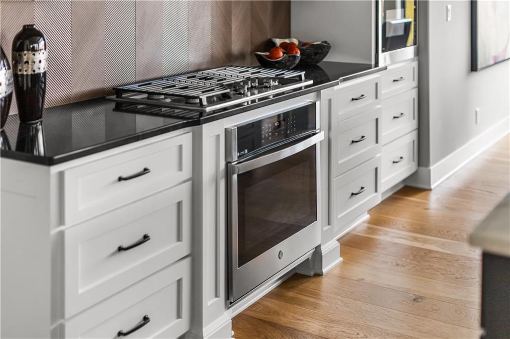 Kitchen with white cabinets, a stainless-steel gas range, black countertops, and patterned backsplash.