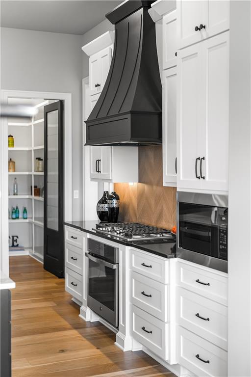 Kitchen with white cabinets, a black range hood, and a herringbone backsplash.