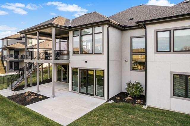 Rear of a two-story home with a balcony, exterior stairs, and a broad paved patio.