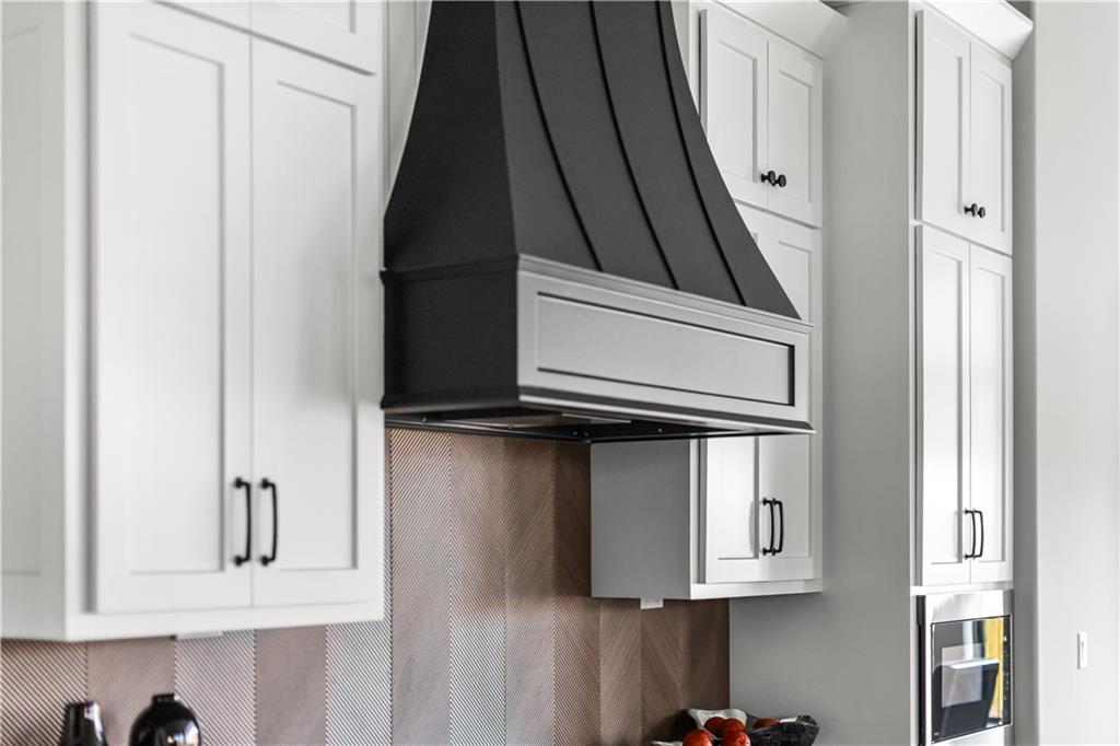Modern kitchen with white cabinets, a black range hood, patterned backsplash, and built-in oven.