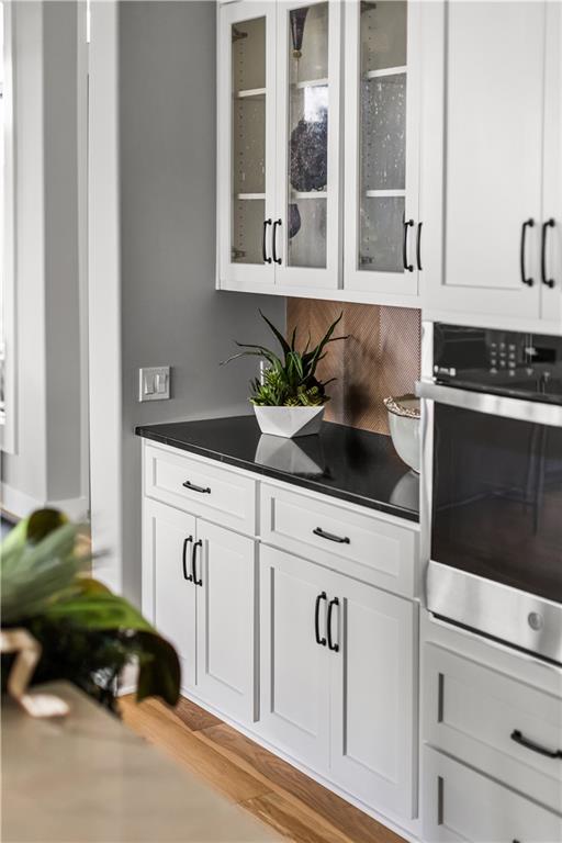 Kitchen with white shaker cabinets, black countertops, and a stainless-steel oven.