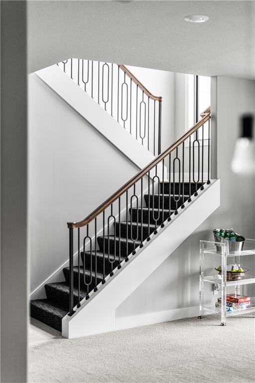 Interior staircase with dark carpeted steps, black metal balusters, and a wooden handrail.