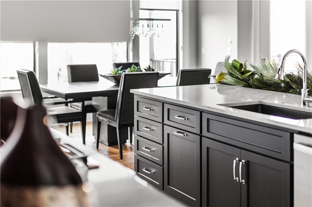 Kitchen island with dark gray cabinets and white countertop, with a dining table and black chairs behind it.
