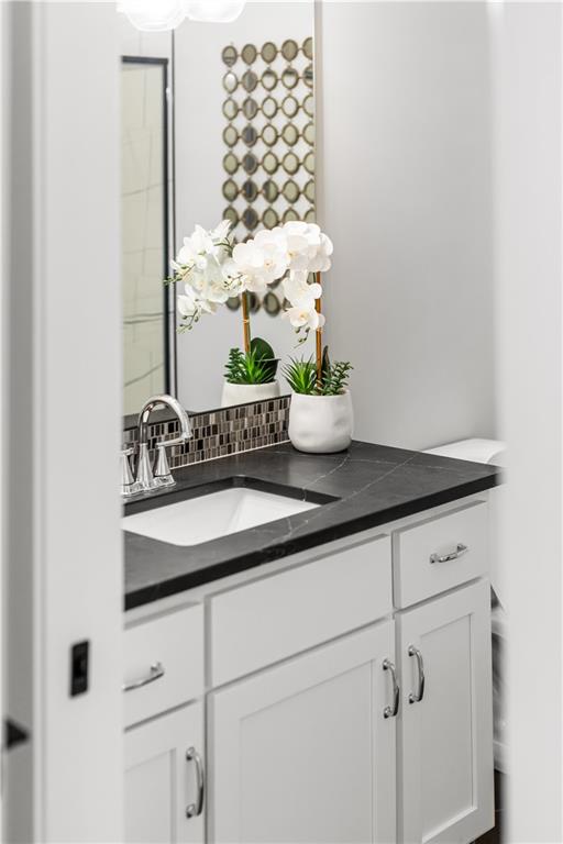Bathroom vanity with dark countertop, chrome faucet, and white orchids beside a decorative mirror.