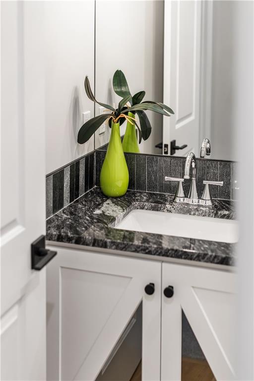 Bathroom vanity with a dark marble counter, white sink, chrome faucet, and green vase with plant.