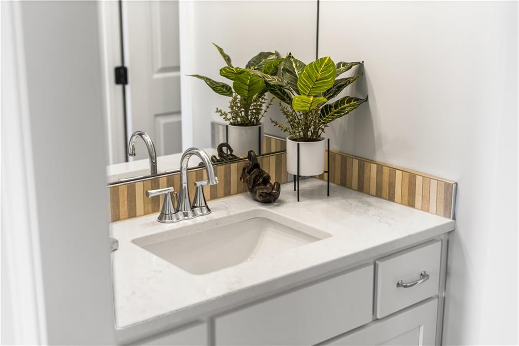 Bathroom vanity with white sink, chrome faucet, striped tile backsplash, and potted plants.