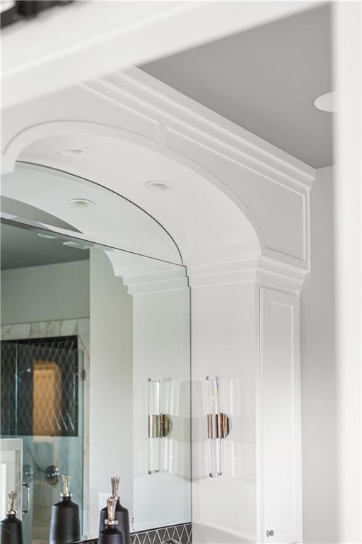 Bathroom vanity with glass sconces, ornate white arch trim, and dark geometric tile.