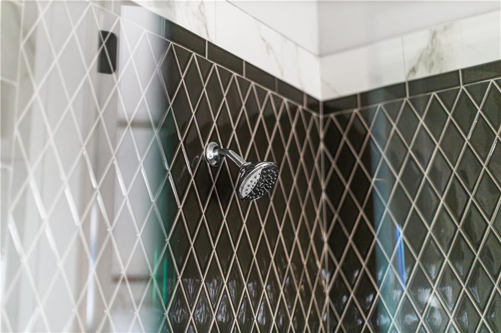 Bathroom shower with chrome showerhead and dark diamond-pattern tile.