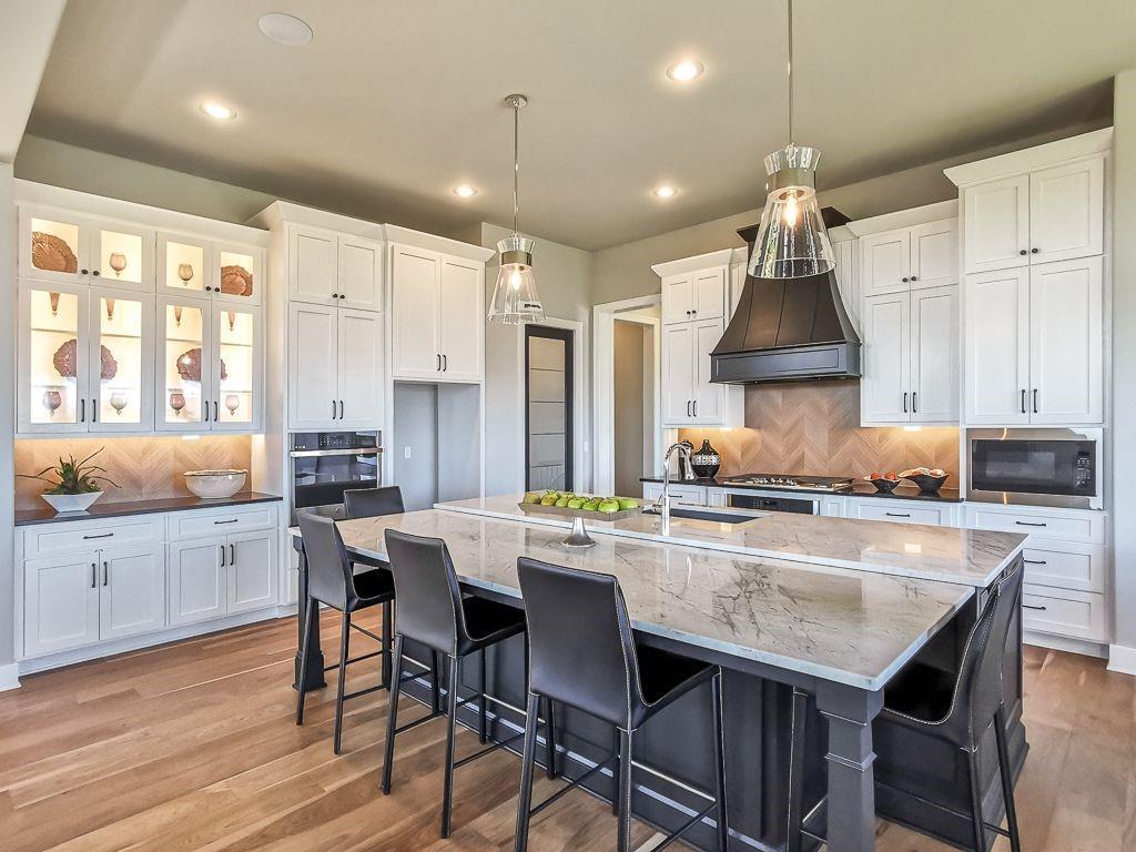 Kitchen with a large marble island, black bar stools, white cabinets, and a herringbone backsplash.