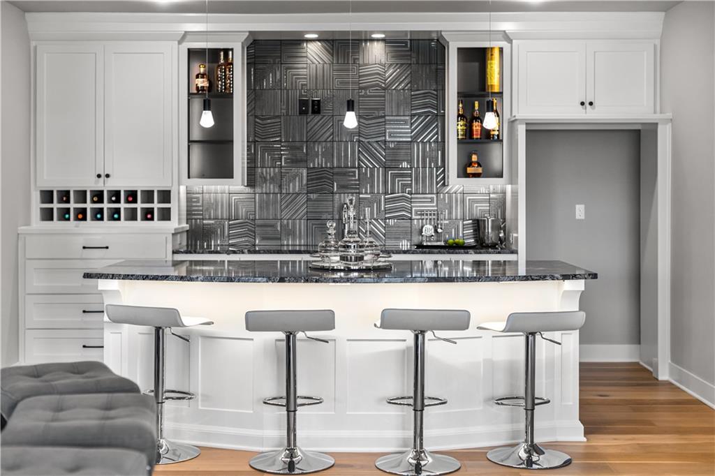 Kitchen with a white island, four bar stools, geometric gray backsplash, and built-in wine storage.