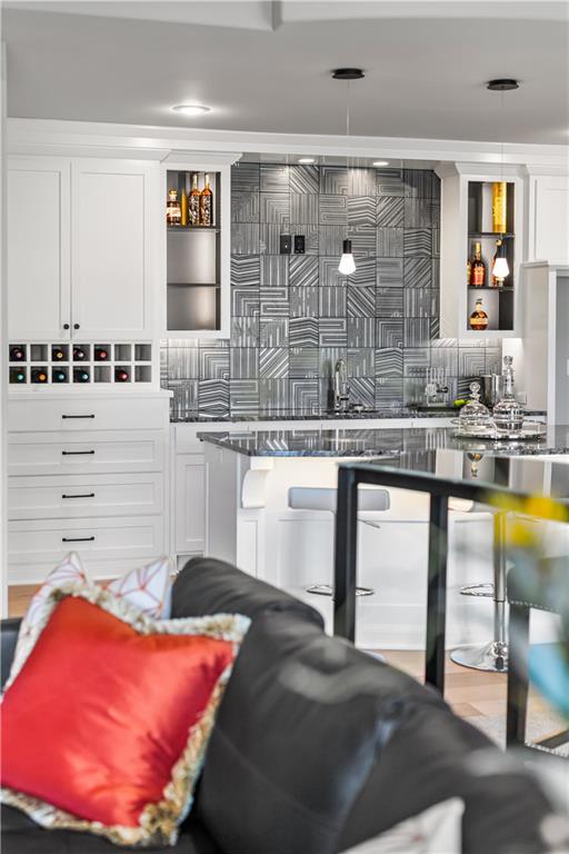 Kitchen with geometric gray tile backsplash, white cabinetry, and island, viewed over a sofa with a red cushion.