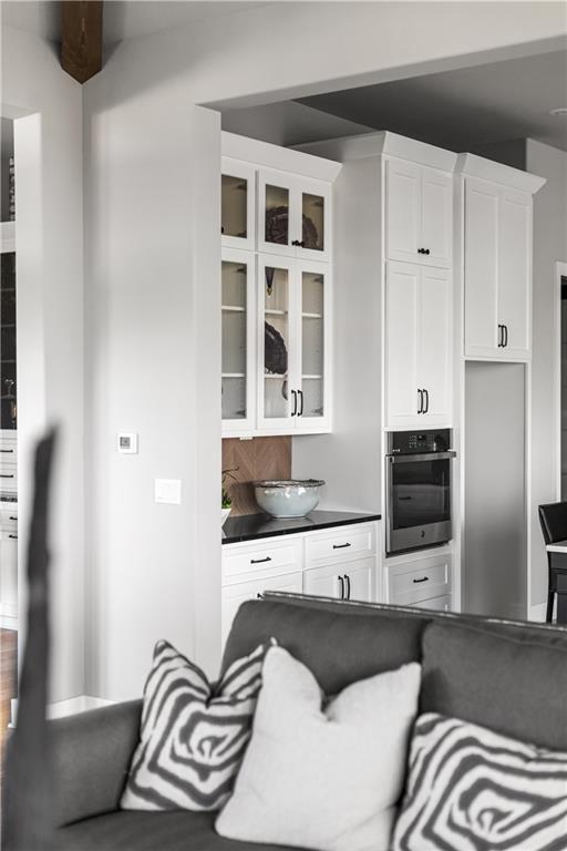 White kitchen with glass-front cabinets and built-in oven, viewed past a gray sofa.