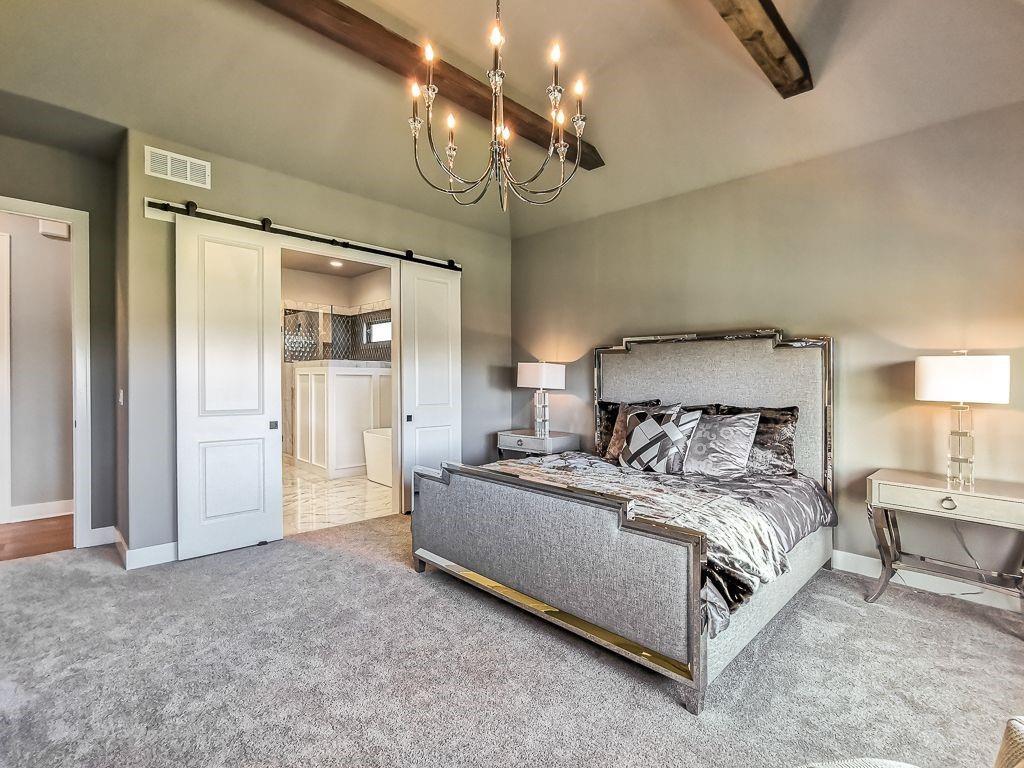 Bedroom with a gray upholstered bed, chandelier, vaulted ceiling, and sliding barn doors opening to a bathroom.