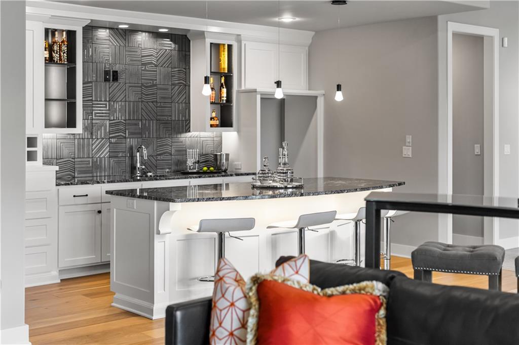 Modern kitchen with stone island, patterned tile backsplash, and bar seating beside living area.