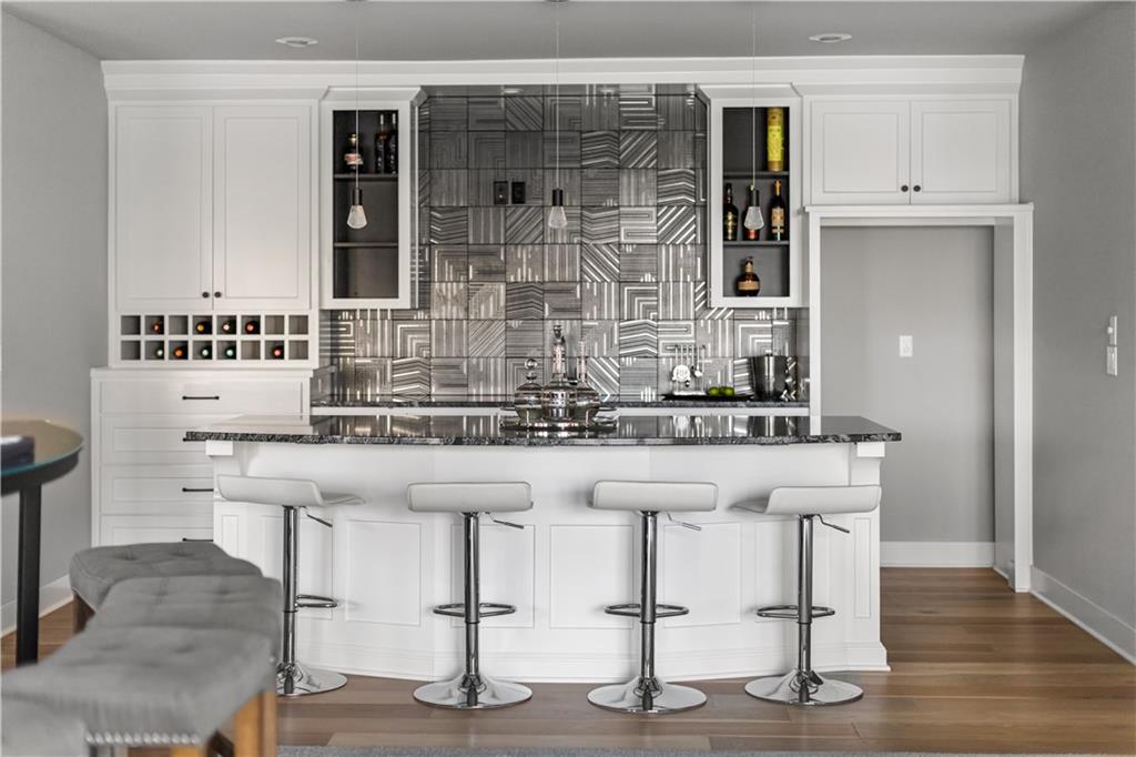 Kitchen bar with geometric metallic tile backsplash, white cabinetry, and four stools at the counter.