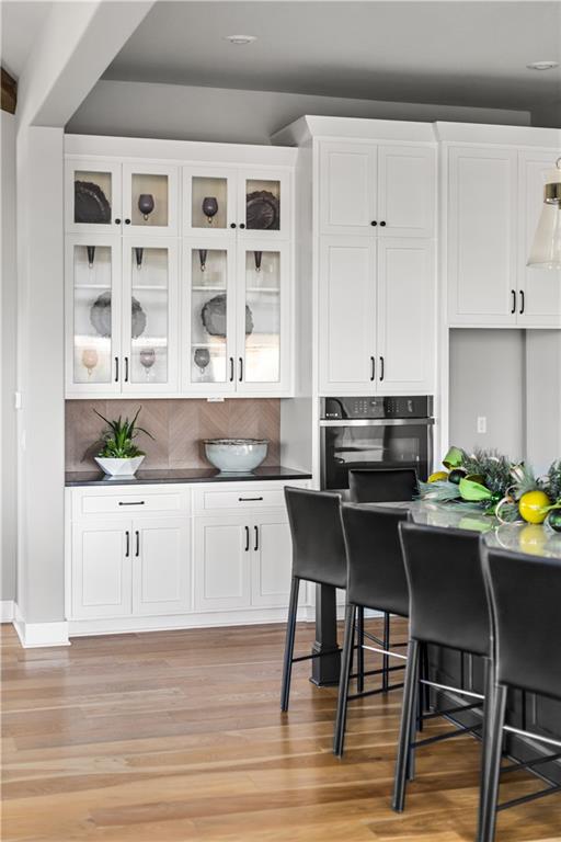 Kitchen with white cabinets, glass-front dish cupboards, built-in oven, and dark island with bar stools.