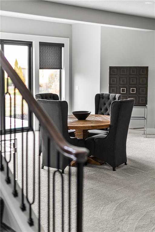 Dining room with a wooden table and dark chairs, viewed past a staircase railing.