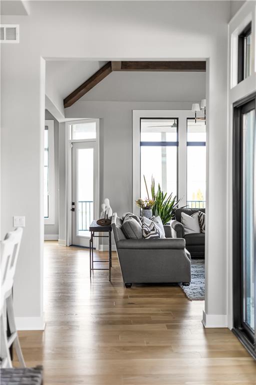 Living room with gray sofas, tall windows, an exposed ceiling beam, and light wood floors.