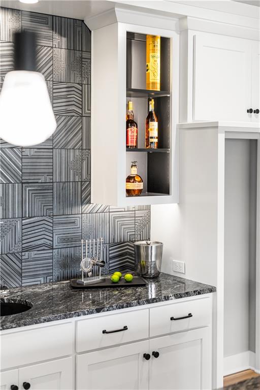 Wet bar with a dark stone counter, geometric tile backsplash, sink, and open liquor cabinet.