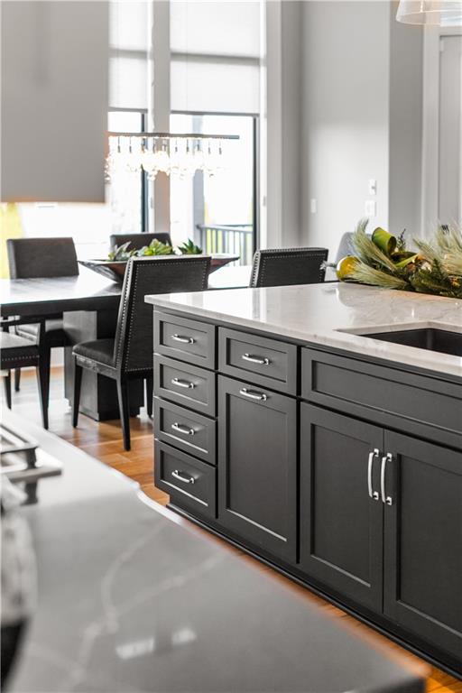 Kitchen with dark cabinetry, a large island, and dining area beside tall windows.