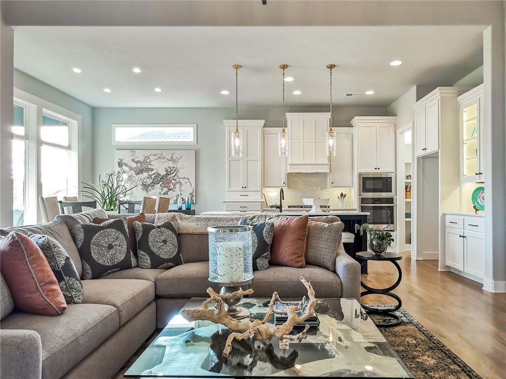 Living room with a sectional sofa facing a glass coffee table, open to a bright white kitchen.