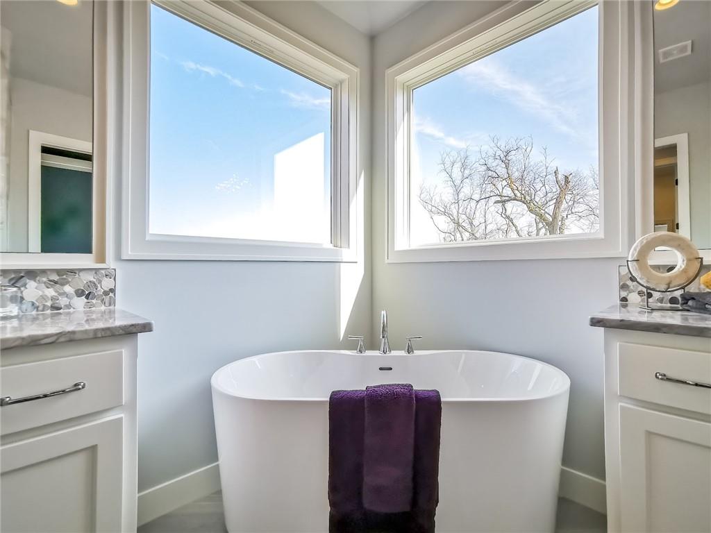 Bathroom with a freestanding tub beneath two large windows, flanked by matching vanities.