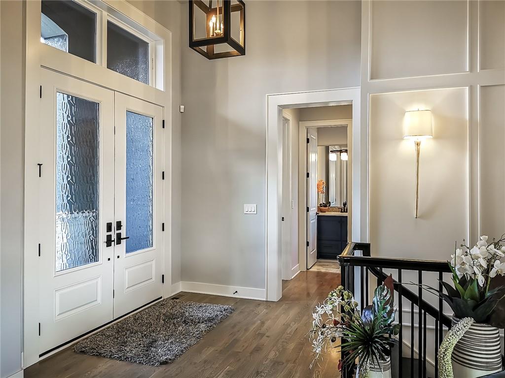 Bright entry foyer with frosted-glass double doors, a wood floor, and a black stair railing.