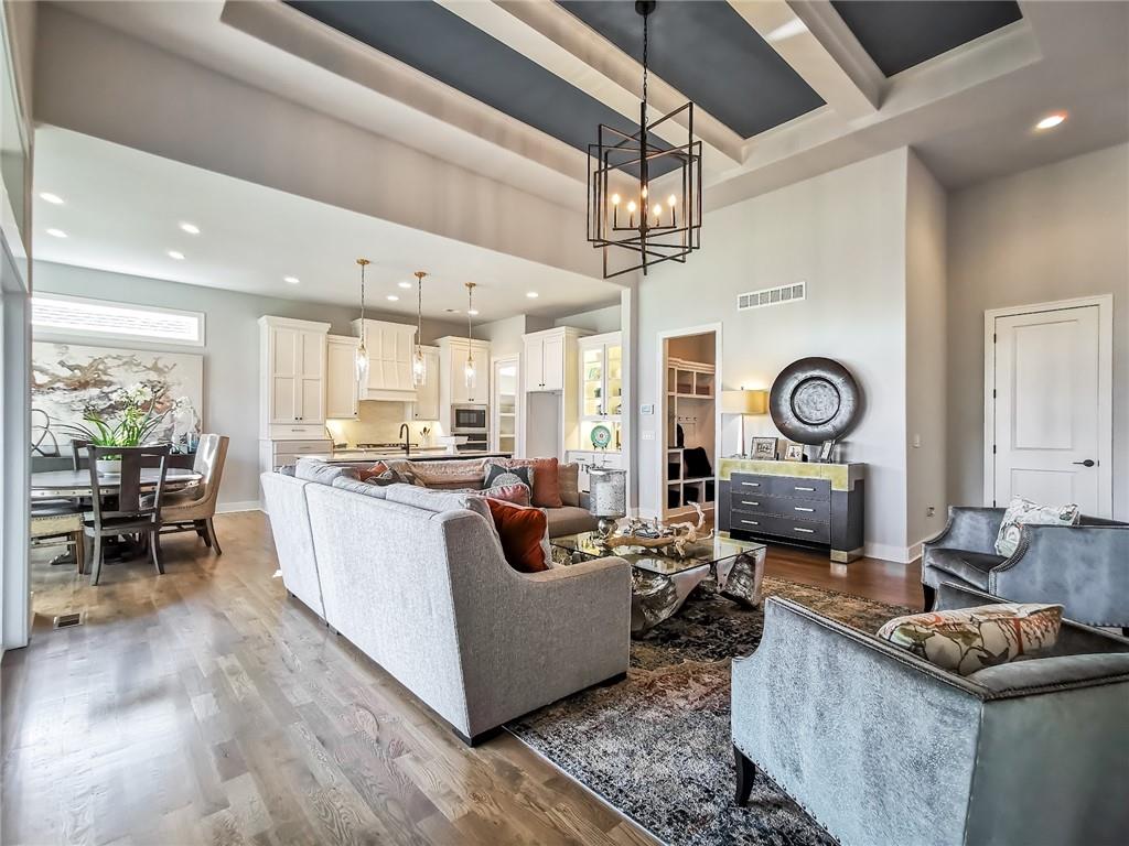 Open-plan living room, dining area, and kitchen with vaulted tray ceiling and modern furnishings.